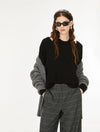 A model wearing a black knit top with gray knit sleeves, paired with gray plaid trousers, a patterned headband, and black sunglasses, against a plain white background.