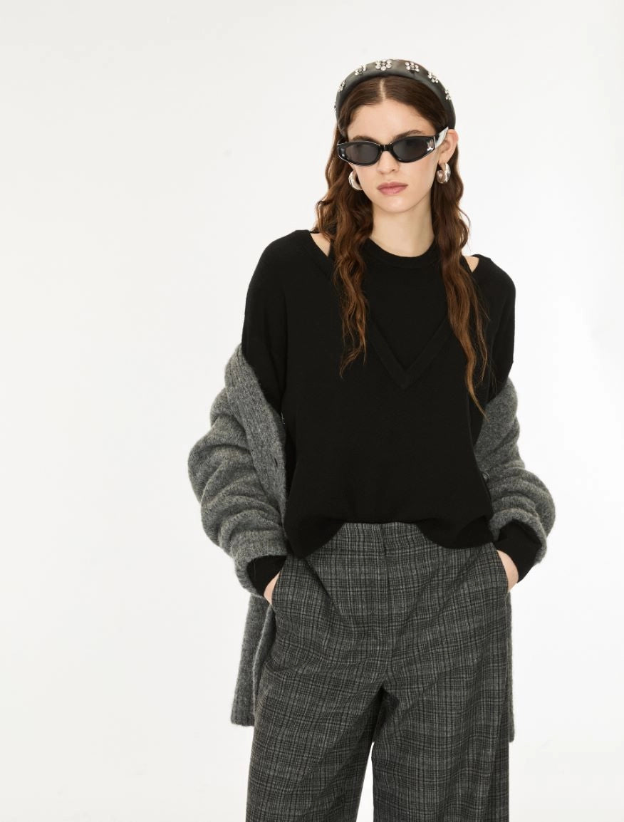 A model wearing a black knit top with gray knit sleeves, paired with gray plaid trousers, a patterned headband, and black sunglasses, against a plain white background.