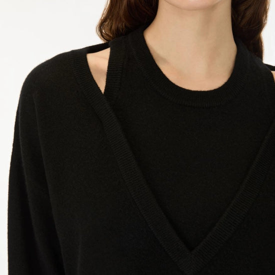 Close-up of a model wearing a black knit sweater with a V-neckline and shoulder cutouts, paired with silver hoop earrings against a plain white background.
