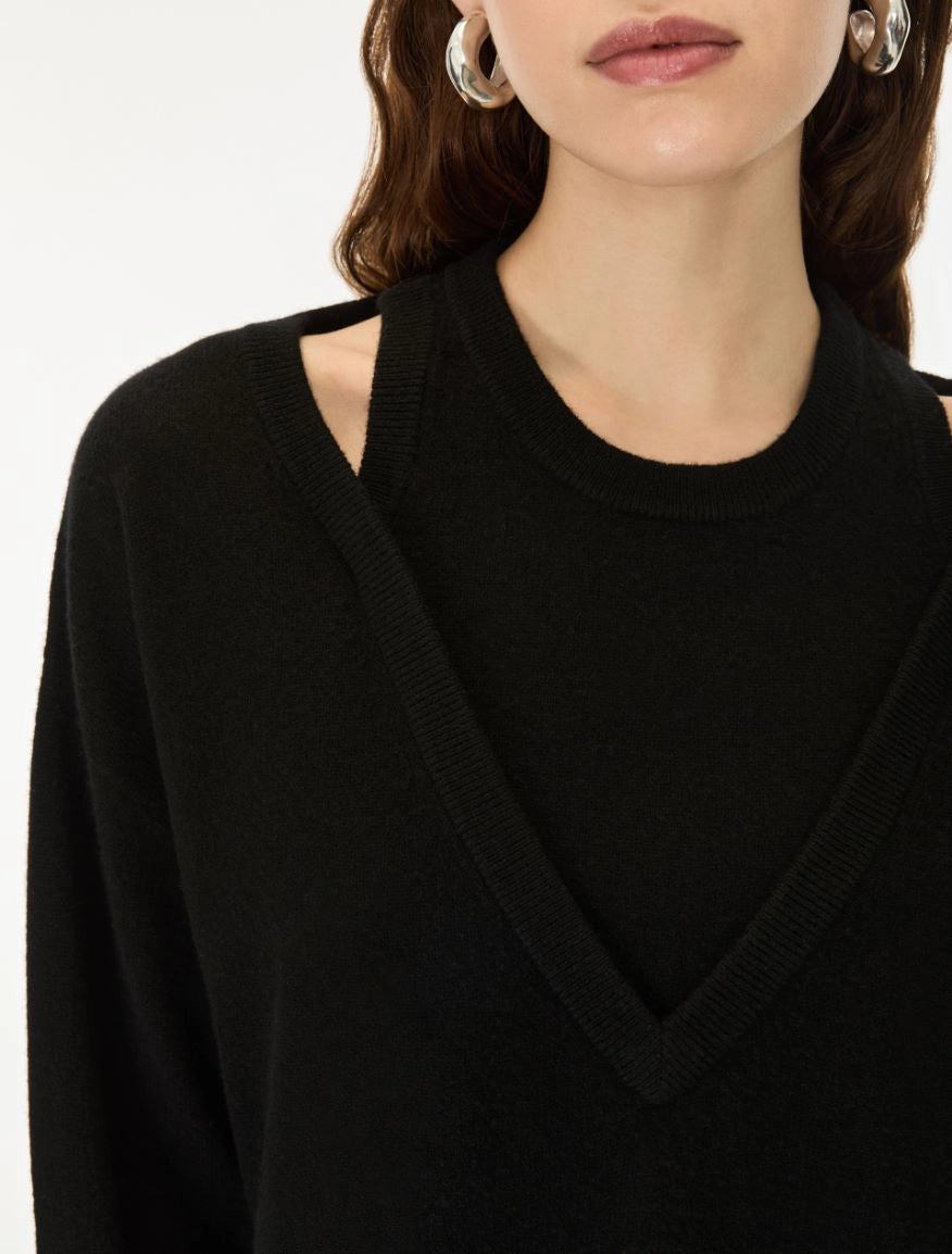 Close-up of a model wearing a black knit sweater with a V-neckline and shoulder cutouts, paired with silver hoop earrings against a plain white background.