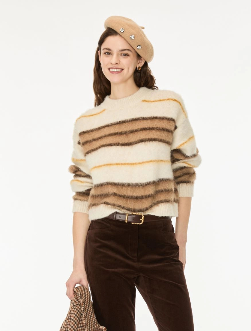 A woman modeling a fuzzy knit sweater with horizontal stripes in cream, brown, and tan, paired with dark brown pants and a beige beret against a plain white background.