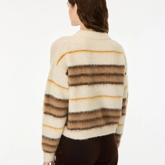 A woman shown from the back wearing a fuzzy knit sweater with horizontal stripes in cream, brown, and tan, paired with dark brown pants, against a plain white background.