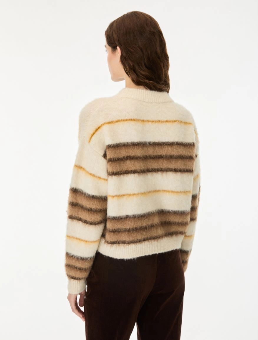 A woman shown from the back wearing a fuzzy knit sweater with horizontal stripes in cream, brown, and tan, paired with dark brown pants, against a plain white background.