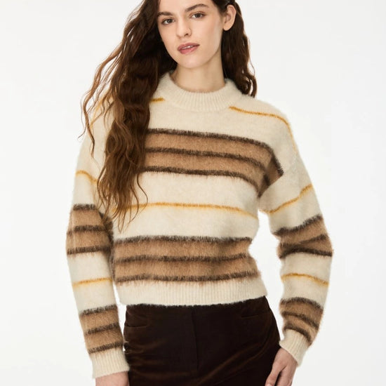 A woman wearing a fuzzy knit sweater with horizontal stripes in cream, brown, and mustard yellow, paired with dark brown pants, against a plain white background.
