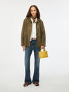 Woman wearing a green jacket, white shirt, blue jeans, and brown shoes, holding a yellow handbag on a white background.