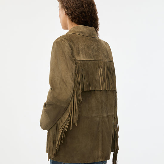 Person wearing a green suede jacket with fringe details on a white background