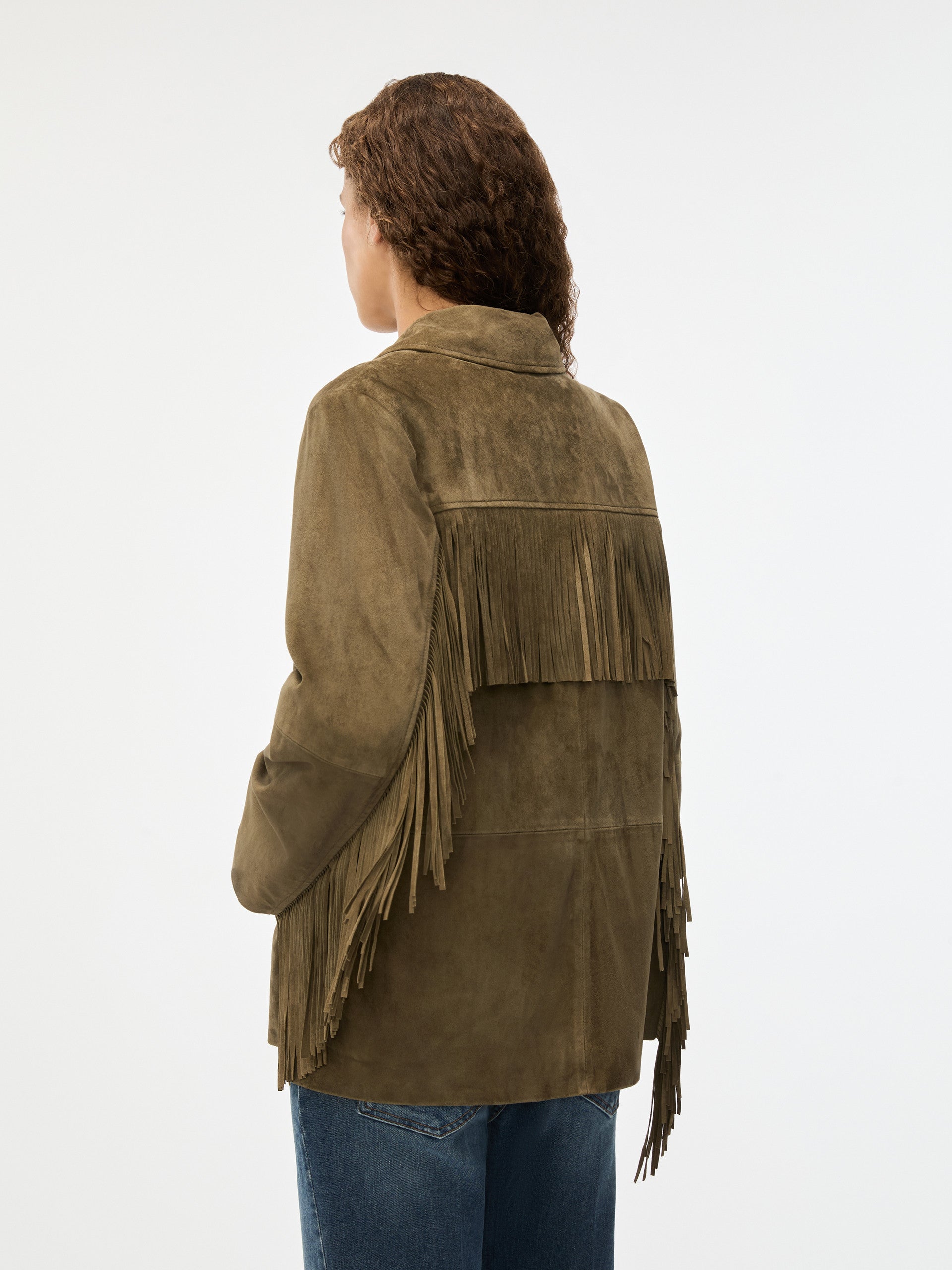 Person wearing a green suede jacket with fringe details on a white background