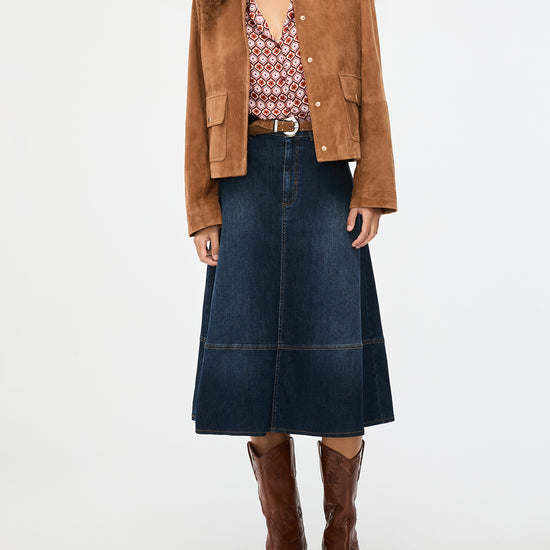 Person wearing a brown jacket, patterned blouse, blue skirt, and brown boots on a white background from iblues