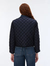 A woman viewed from the back wearing a dark navy quilted jacket and blue jeans against a plain white studio background.
