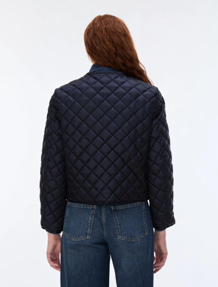 A woman viewed from the back wearing a dark navy quilted jacket and blue jeans against a plain white studio background.