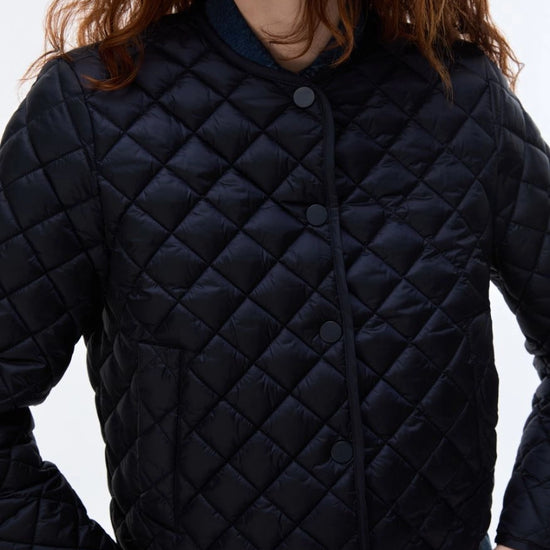 A close-up of a person wearing a dark navy quilted puffer jacket with a diamond-stitched pattern and snap-button front closure, set against a plain light background.