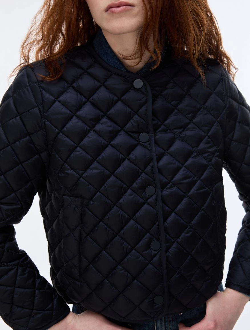 A close-up of a person wearing a dark navy quilted puffer jacket with a diamond-stitched pattern and snap-button front closure, set against a plain light background.