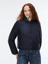 A model with red hair wearing a dark navy blue cropped puffer jacket with a stand-up collar and front buttons, paired with blue jeans with silver studs, against a plain white studio background.