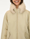 A close-up of a person wearing a beige winter parka with a fluffy cream faux-fur collar and a front zipper, against a plain light background.