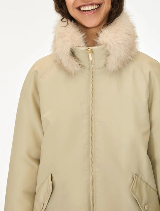 A close-up of a person wearing a beige winter parka with a fluffy cream faux-fur collar and a front zipper, against a plain light background.
