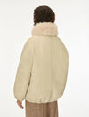 A person shown from the back wearing a cream-colored puffer jacket with a fluffy light beige faux-fur collar, paired with brown and beige checkered trousers, against a plain white studio background.