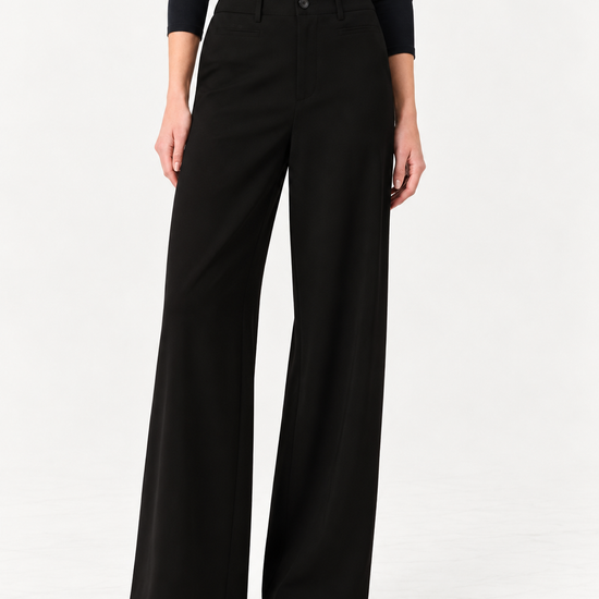 A model wearing black wide-leg trousers and a black long-sleeve top, standing against a plain white studio background.