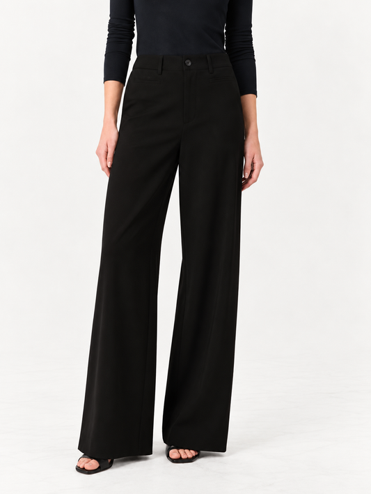 A model wearing black wide-leg trousers and a black long-sleeve top, standing against a plain white studio background.