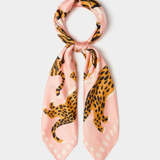 A pink silk scarf featuring a leopard print pattern with black and orange spots, tied in a loop at the top and displayed against a light gray background.