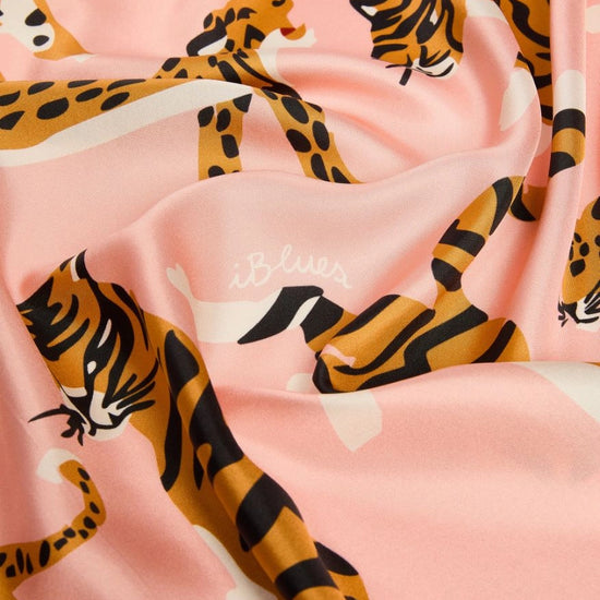 A close-up of a pink fabric with a repeating print of orange and black tiger and leopard animals, plus small white script logos.