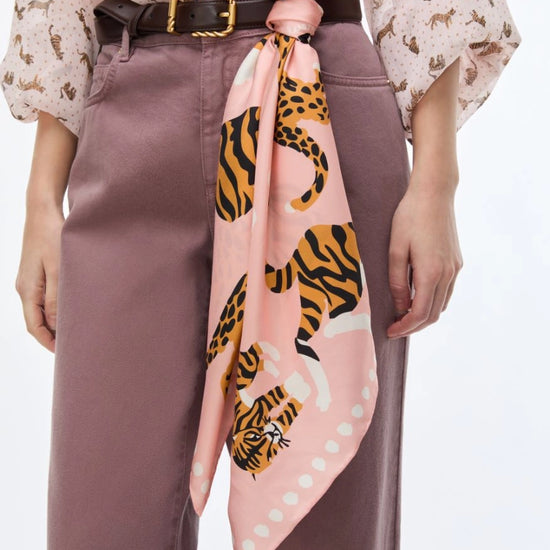 A pink silk scarf with a tiger and leopard print, tied around a model's waist over a mauve dress and a black belt.