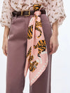 A pink silk scarf with a tiger and leopard print, tied around a model's waist over a mauve dress and a black belt.