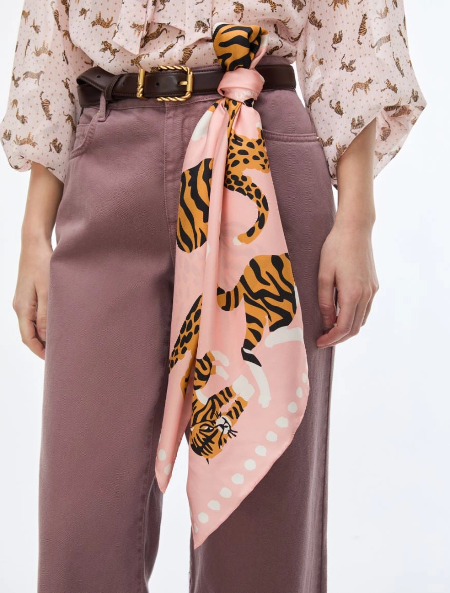 A pink silk scarf with a tiger and leopard print, tied around a model's waist over a mauve dress and a black belt.