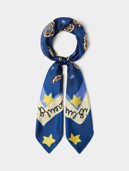 A blue silk scarf with a celestial print featuring yellow stars, a cream banner with black cursive text, and gold-toned ornamental details, shown on a light gray background.