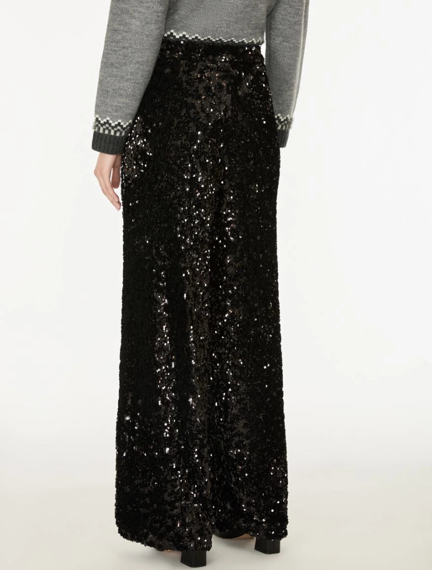 A person wearing a long black sequined maxi skirt with a gray long-sleeve top featuring a black and white patterned knit cuff, shown from the back against a plain white studio background.