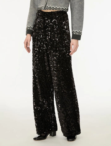 A model is shown from the waist down wearing high-waisted, wide-leg black sequined trousers paired with a gray cropped sweater and black shoes, set against a plain white studio background.