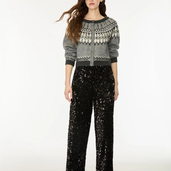 A model wearing a gray knit cardigan with a white geometric pattern on the yoke, paired with black wide-leg sequined pants, against a plain white studio background.