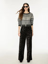 A model wearing a gray knit cardigan with a white geometric pattern on the yoke, paired with black wide-leg sequined pants, against a plain white studio background.