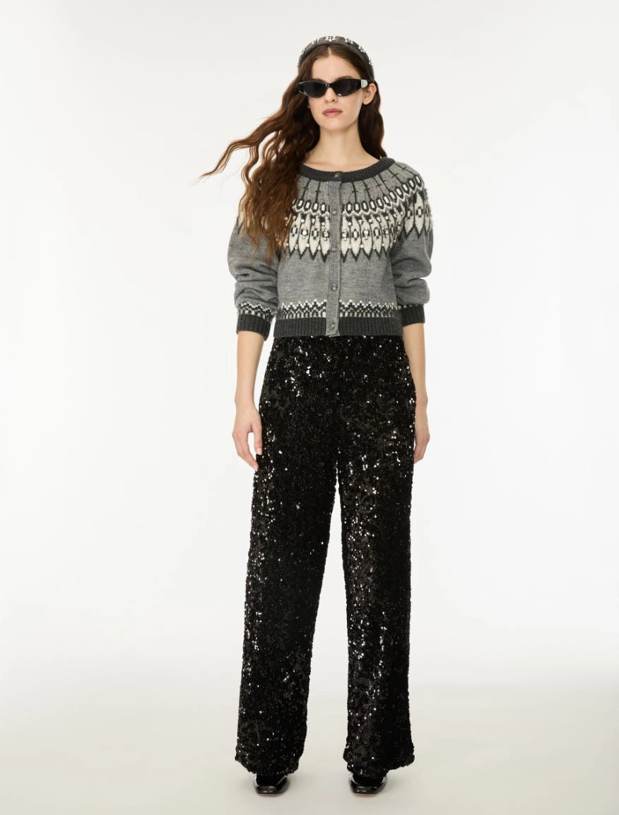 A model wearing a gray knit cardigan with a white geometric pattern on the yoke, paired with black wide-leg sequined pants, against a plain white studio background.