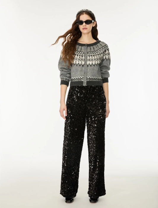 A model wearing a gray knit cardigan with a white geometric pattern on the yoke, paired with black wide-leg sequined pants, against a plain white studio background.