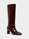 A single knee-high boot in a glossy deep burgundy leather, featuring a pointed toe and a chunky block heel, shown against a plain light gray background.