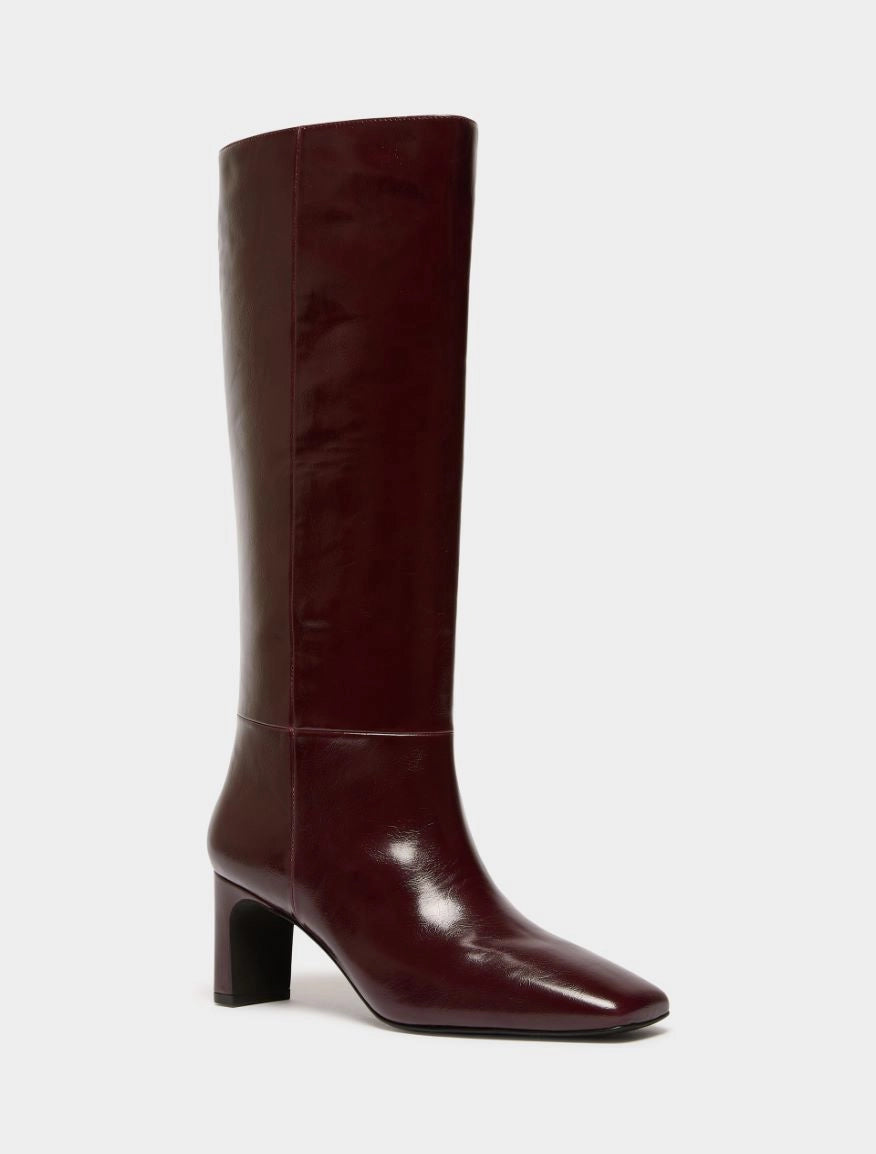 A single knee-high boot in a glossy deep burgundy leather, featuring a pointed toe and a chunky block heel, shown against a plain light gray background.