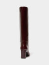 A single knee-high boot in a glossy deep burgundy leather, shown from a rear three-quarter view against a solid off-white background.