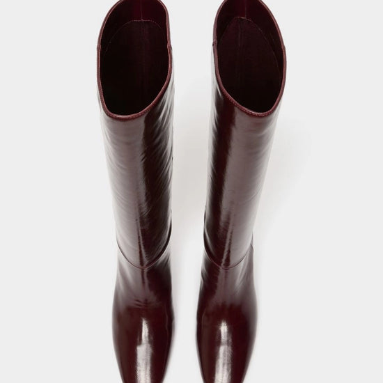 A pair of glossy, knee-high boots in a deep burgundy color, shown from a top-down view against a plain light gray background.