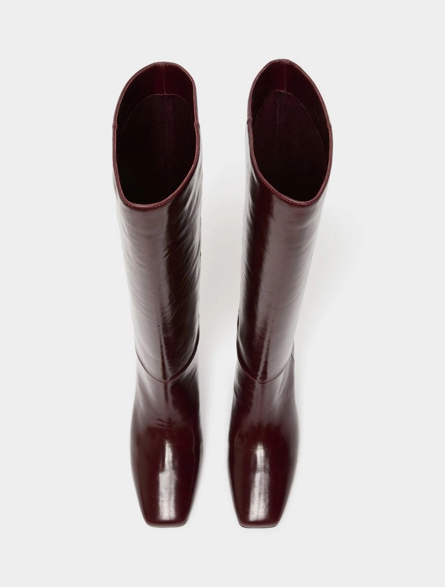 A pair of glossy, knee-high boots in a deep burgundy color, shown from a top-down view against a plain light gray background.