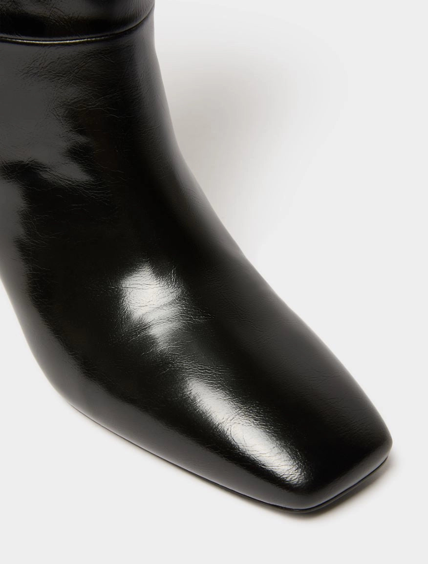 Close-up of a glossy black leather ankle boot with a square toe on a clean white background.