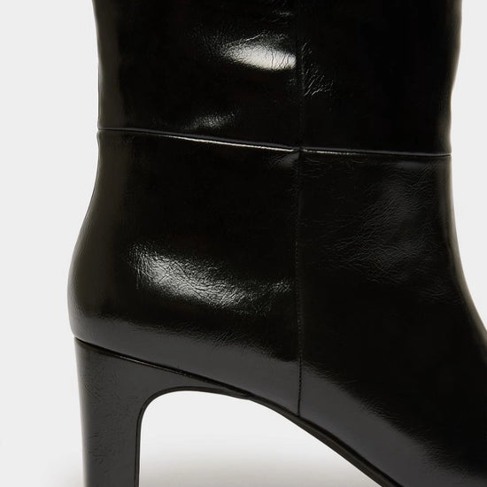 Close-up of a black leather knee-high boot with a block heel, showing the side profile and smooth glossy finish against a light gray background.