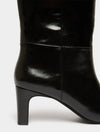 Close-up of a black leather knee-high boot with a block heel, showing the side profile and smooth glossy finish against a light gray background.