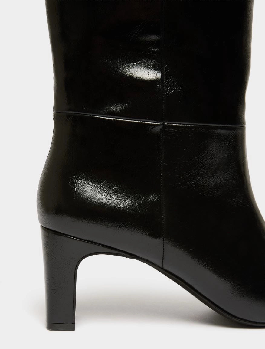 Close-up of a black leather knee-high boot with a block heel, showing the side profile and smooth glossy finish against a light gray background.