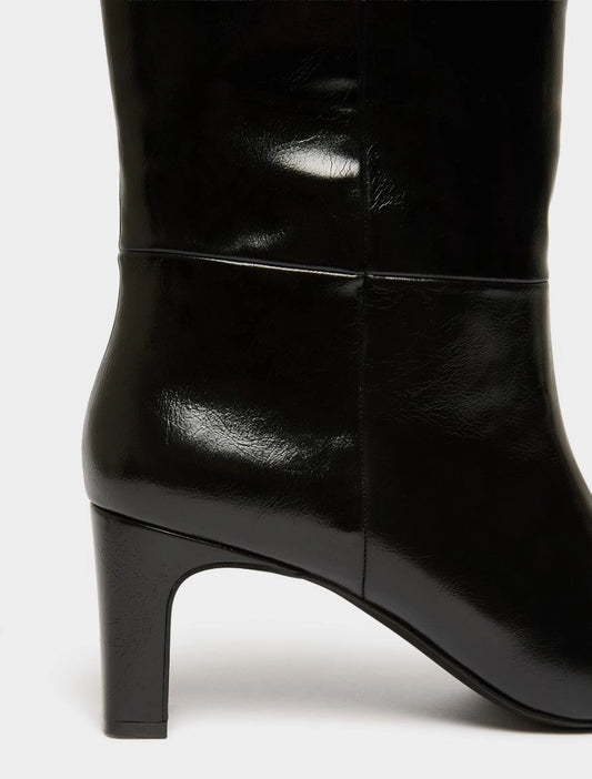 Close-up of a black leather knee-high boot with a block heel, showing the side profile and smooth glossy finish against a light gray background.