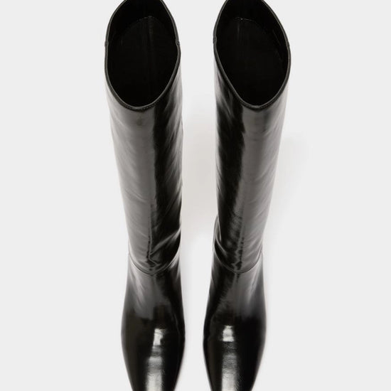 A pair of glossy black knee-high boots with a pointed toe and low block heel, shown from a top-down view on a light gray background.