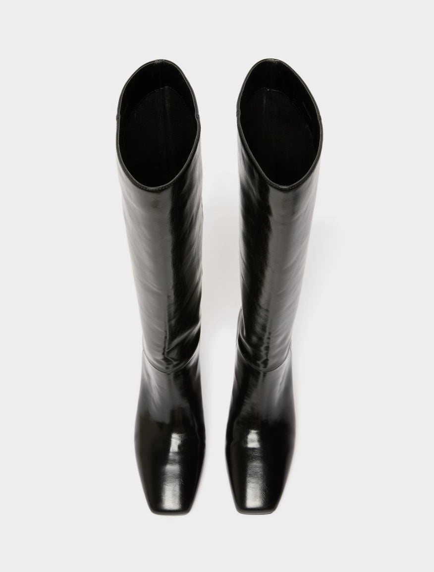 A pair of glossy black knee-high boots with a pointed toe and low block heel, shown from a top-down view on a light gray background.