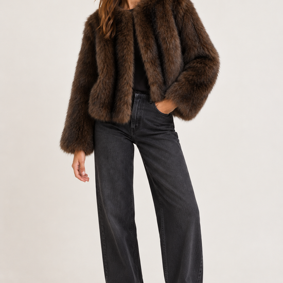 A woman modeling a dark brown fur jacket, styled with black wide-leg jeans and black pointed-toe heels, against a plain light gray studio background.