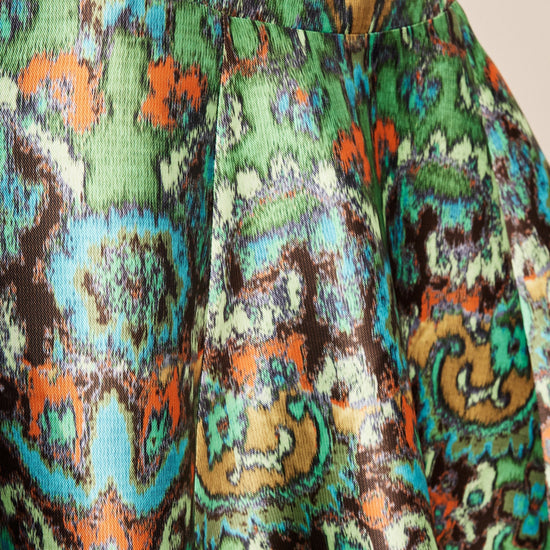 Close-up of a pleated skirt with a vibrant, multicolor abstract paisley pattern featuring green, orange, blue, brown, and black.