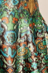 Close-up of a pleated skirt with a vibrant, multicolor abstract paisley pattern featuring green, orange, blue, brown, and black.