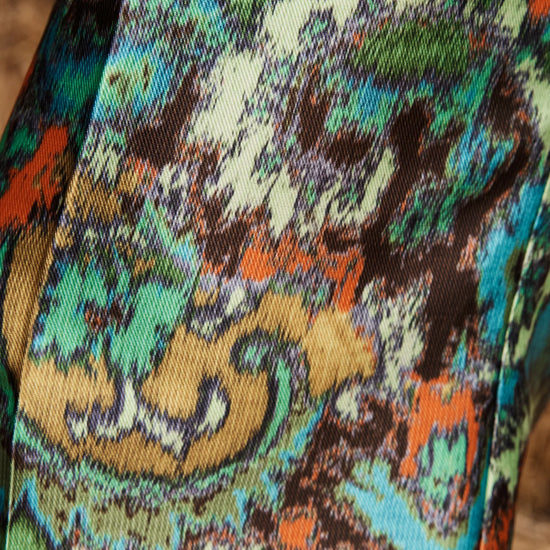 A close-up of a colorful paisley patterned fabric with swirling motifs in green, teal, orange, brown, beige, and white.